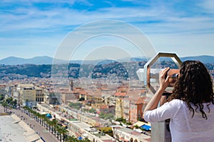 girl tourist on coin operated binocular from behind, enjoying looking at panoramic view of Nice, France