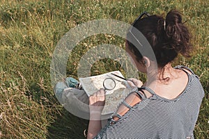 Girl tourist examines through a magnifying glass something on a map with a pen in his hand