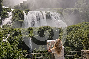 Girl tourist looks through binoculars at a waterfall Cascata delle Marmore in Italy