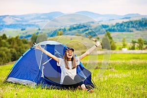 Girl tourist meets morning with outstretched arms in tent with beautiful mountains view