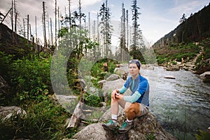 Turistická dívka Sedin na kameni u horské řeky ve Vysokých Tatrách na Slovensku. Oblečená v modrém tričku, šedých šortkách, Turistika