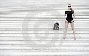 Girl tourist stand stony stairs near her backpack. Ready to explore new city. Woman sunglasses stylish black outfit