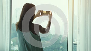 Girl tourist standing at thepanoramic window and photographed on a mobile phone view of a skyscraper height in Kuala