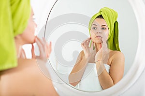 Girl with a towel on her head looks in mirror