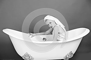 Girl with towel turban sitting in white bathtub