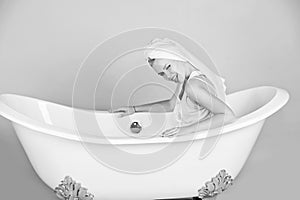 Girl with towel turban sitting in white bathtub