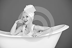 Girl with towel turban sitting in white bathtub