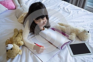 Girl with toys writing in book on bed