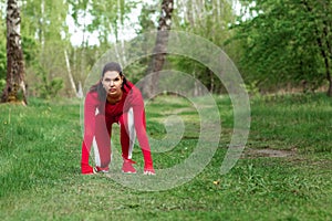 A girl in a tracksuit is preparing to run, physical exercises against the backdrop of nature, prelaunch pose. The concept of a photo