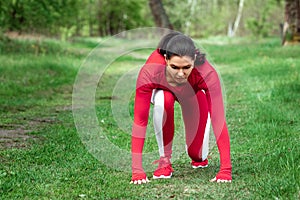 A girl in a tracksuit is preparing to run, physical exercises against the backdrop of nature, prelaunch pose. The concept of a photo