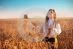 Girl with traditional Bulgarian folklore costume at the agricultural wheat field during harvest time with industrial combine