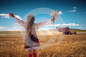 girl with traditional Bulgarian folklore costume at the agricultural wheat field during harvest time with industrial combine