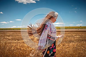 Girl in traditional ethnic folklore costume with Bulgarian embroidery standing on a harvest golden wheat field