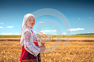 Girl in traditional ethnic folklore costume with Bulgarian embroidery standing on a harvest golden wheat field