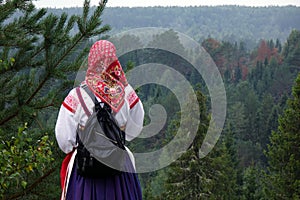 Girl in a traditional folk costume in nature, looking into the distance. Green pine forest.