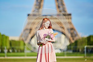 Girl with traditional French bread baguette and flowers in front of the Eiffel tower