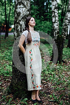 Girl in traditional Russian dress sarafan leaned against birch