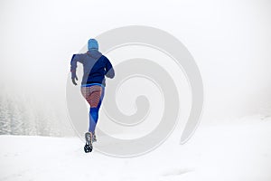 Girl trail running on snow in winter mountains