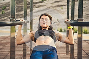 Girl trains outdoors in street gym. Training of biceps and triceps. woman parallel bars workout exercise. female athlete