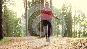 Girl trains with a skipping rope in a summer Park on sunset. young woman doing sports outdoors. slow motion