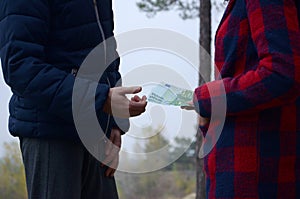 Girl transfers euro bills to the hands of a young guy in forest. Concept of robbery or illegal deal transaction