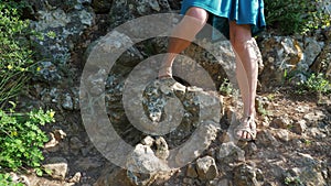 A girl traveler in a blue skirt and sandals descends a steep mountain slope.