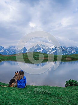 A girl traveler and a dog sit on the shore of the mountain lake Koruldi, Georgia, Svaneti