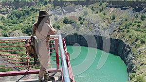 girl traveler in a hat and a backpack makes a photo near a kimberlite pipe