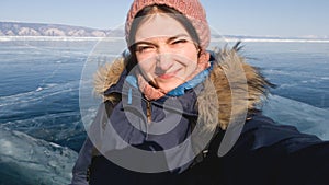 Girl traveler makes a selfie on the winter lake Baikal. The lake in the ice. The sun is bright, the girl wrinkles her nose