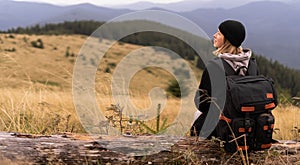 girl traveler in the mountain is resting sitting on a wooden log, traveling through the Alps, woman tourist is resting