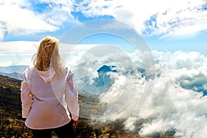 Girl is a traveler in a mountain trek. A view from above on mountains and clouds. Above the clouds. Trekking to Rinjani volcano.