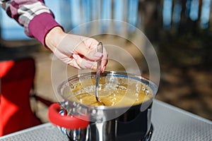 Girl traveler prepares food on portable gas stove, on a folding table on the background of camping in forest. Women's hands inter