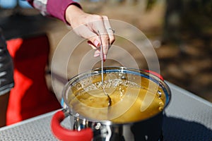 Girl traveler prepares food on portable gas stove, on a folding table on the background of camping in forest. Women's hands inter