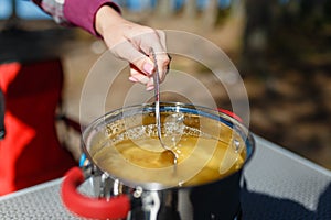 Girl traveler prepares food on portable gas stove, on a folding table on the background of camping in forest. Women's hands inter