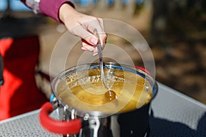 Girl traveler prepares food on portable gas stove, on a folding table on the background of camping in forest. Women's hands inter