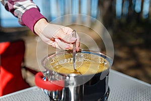 Girl traveler prepares food on portable gas stove, on a folding table on the background of camping in forest. Women's hands inter