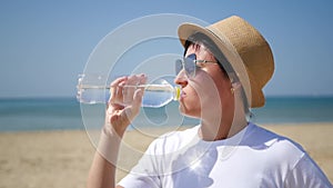 Girl traveler quenches thirst in a sunny hot day standing on the beach. A woman drinks clean drinking water from a