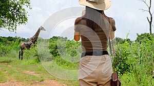 girl traveler in safari style photographs a giraffe in the savannah