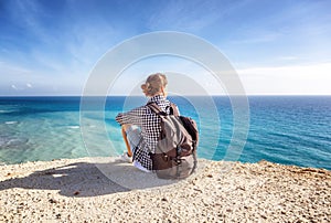 A girl traveler sits on a rock and admires the blue boundless se