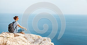 A girl traveler sits on a rock and admires the blue boundless se