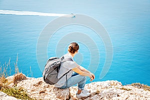 A girl traveler sits on a rock and admires the blue boundless se