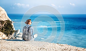 A girl traveler sits on a rock and admires the blue boundless se