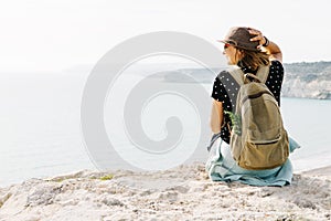 A girl traveler sits on a rock and admires the blue sea, freedom