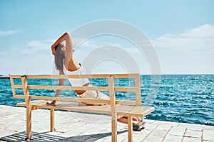 Girl traveler sitting on bench near the beach looking sea