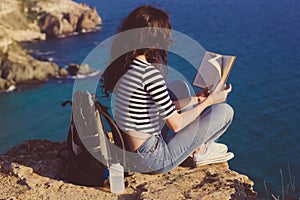 Girl traveler is sitting on mountain peak and reading book