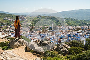 Girl traveler sitting in the top of a hill watching over Chefchaouen, the blue city