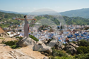 Girl traveler sitting in the top of a hill watching over Chefchaouen, the blue city, Morocco