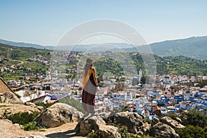 Girl traveler sitting in the top of a hill watching over Chefchaouen, the blue city, Morocco