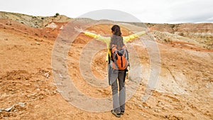 A girl traveler stands in a desert mountainous area near the red rocks of Kyzyl Chin in the Altai in Russia. Backpack