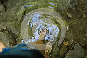 Girl at the waterfall in the woods touching the water with his foot